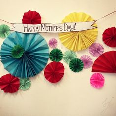 colorful paper fans are hanging on the wall with a sign that says happy mother's day