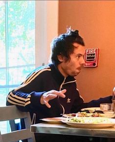 a man sitting at a table in front of a plate of food with his hands out