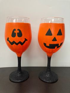 two wine glasses decorated with jack - o'- lantern faces are sitting on a table