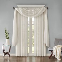 a living room filled with furniture and a window covered in white drapes next to a chair