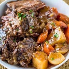 a white bowl filled with meat and potatoes on top of a tablecloth covered table