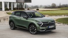 a green suv parked in front of a large building with grass and bushes behind it