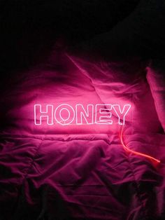 a neon sign that reads honey on top of a purple bed with a black comforter