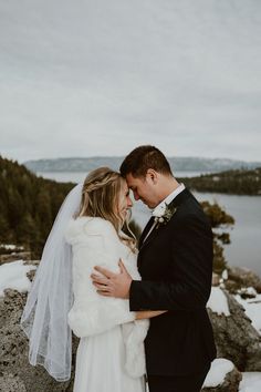 a bride and groom embracing each other in front of snow covered rocks by the water