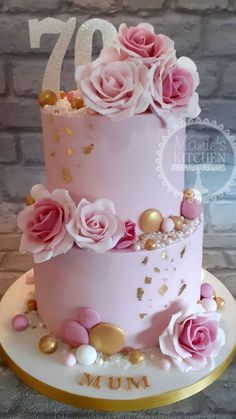 a pink and gold cake with flowers on it's top is displayed in front of a brick wall