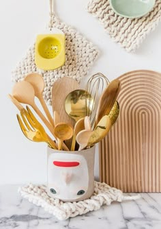 kitchen utensils and spoons in a cup on a marble counter top next to wall art