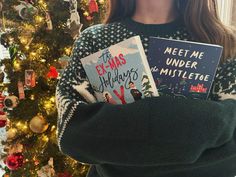 a woman holding two books in front of a christmas tree