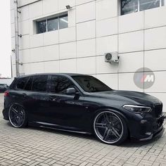 a black bmw is parked in front of a white brick building with its door open