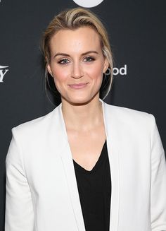 a woman wearing a white blazer and black top smiles at the camera while standing in front of a red carpet