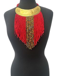 This authentic African necklace boasts a beautiful red beaded design with tassel fringe accents. The intricate brass pendant adds a touch of elegance to this statement piece, making it the perfect addition to your ethnic jewellery collection. The necklace has been expertly crafted in Africa and showcases the vibrant and unique culture of the region. It is ideal for those who love to add ethnic and tribal styles to their wardrobe. Material:  Beads and decorative brass metal. Fringe - 9ins/22cm Neck Width - 18ins/46cm Colour: Red Weight: 200g Gold Tassel Necklaces For Festival, Gold Tassel Necklace For Festivals, Traditional Gold Fringe Jewelry, Red Tassel Necklaces For Gifts, Red Tassel Necklaces As Gifts, Bohemian Gold Beaded Necklaces With Tassels, Red Tassel Necklace For Gift, Traditional Red Jewelry With Tassels, Bohemian Gold Necklace With Beaded Fringe