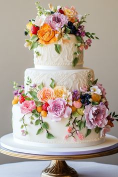 a three tiered wedding cake with colorful flowers on the top and bottom, sitting on a gold pedestal