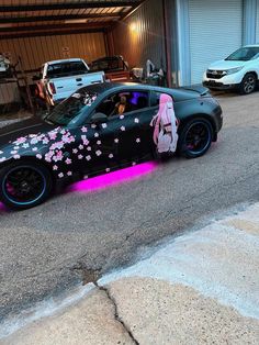 a car with pink flowers painted on it's side in front of a garage