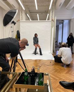 two people are taking pictures in front of a white backdrop while another person is sitting on the floor