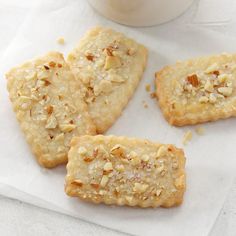 four cookies with nuts on top sitting next to a cup of coffee and napkins