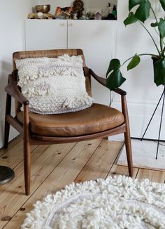 a chair with a pillow sitting on top of it next to a lamp and potted plant