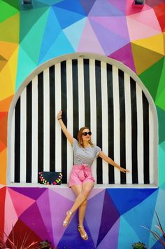 a woman sitting on the side of a colorful building with her arms in the air