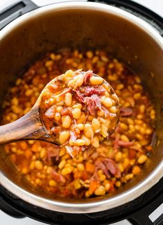 a wooden spoon full of beans and ham cooking in a crock pot on the stove