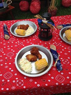 two plates with corn on the cob and mashed potatoes are sitting on a red tablecloth