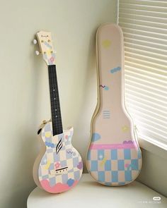 two guitars are sitting next to each other on a shelf in front of a window