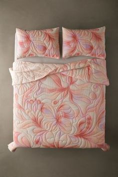 a bed with pink and white comforter set on top of the bed in front of a gray wall