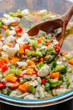 a bowl full of vegetables being stirred with a wooden spoon