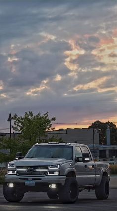 a silver truck parked in a parking lot with the sun setting behind it and clouds