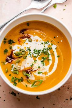 a white bowl filled with carrot soup and topped with sour cream, green onions and parsley