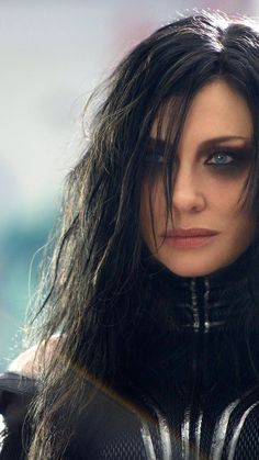 a close up of a woman with dark hair and black leather clothes, looking at the camera