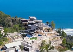 an aerial view of a large house on the shore with blue water in the background