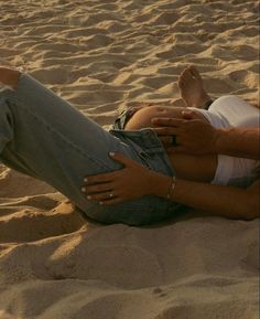 a man and woman are laying on the sand at the beach with their arms around each other