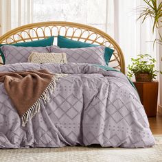 a bed with purple and teal comforters in front of a window, next to potted plants