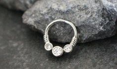 a silver nose ring with three stones on it's end, sitting on top of some rocks