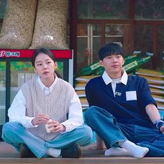 two young people sitting on the ground in front of a store with their hands together