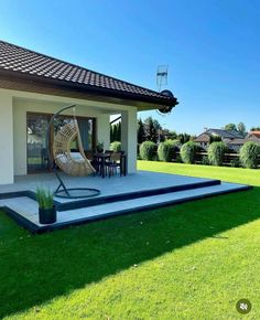 a house with grass and lawn furniture in the front yard, next to a patio