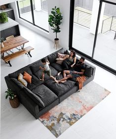 three adults and two children sitting on a couch in a living room with large windows