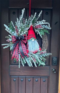 a wreath with two gnomes on it hanging from the front door to welcome guests