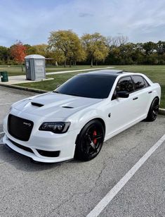 a white car parked in a parking lot next to some grass and trees on the other side