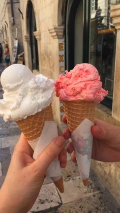 two ice cream cones are being held up in front of an old building on the street