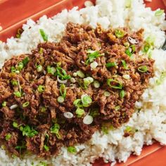 a red plate topped with rice covered in meat and scallions next to a fork