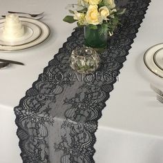 the table is set with white and yellow flowers in a vase on top of black lace