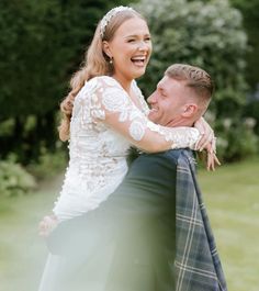 a man and woman hugging each other in front of green grass with trees behind them