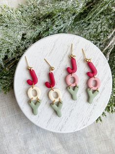 four pairs of earrings on top of a white plate next to green and red plants