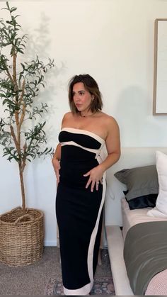 a woman in a black and white dress standing next to a bed with a potted plant