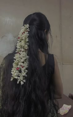 the back of a woman's head with flowers in her long black hair, sitting on a table