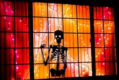 a skeleton is standing in front of a window decorated with christmas lights and garlands