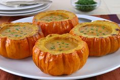 four pumpkins with soup in them on a white plate next to plates and silverware