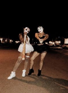 two women dressed up as clowns in the street at night with one holding a bat