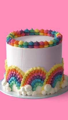 a rainbow cake with white frosting on a pink background