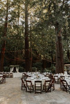 the tables are set up for an outdoor wedding in the woods with string lights strung from the trees