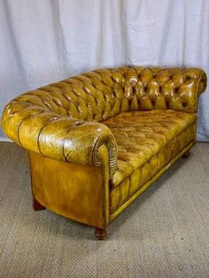 a brown leather couch sitting on top of a carpeted floor next to a white curtain